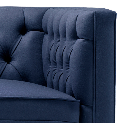 Close-up of a dark blue upholstered sofa with tufted back cushion and armrest.