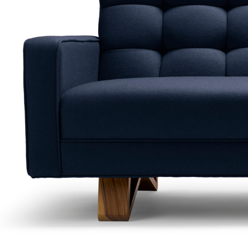 Close-up of a navy blue modern sofa with tufted backrest and wooden legs.