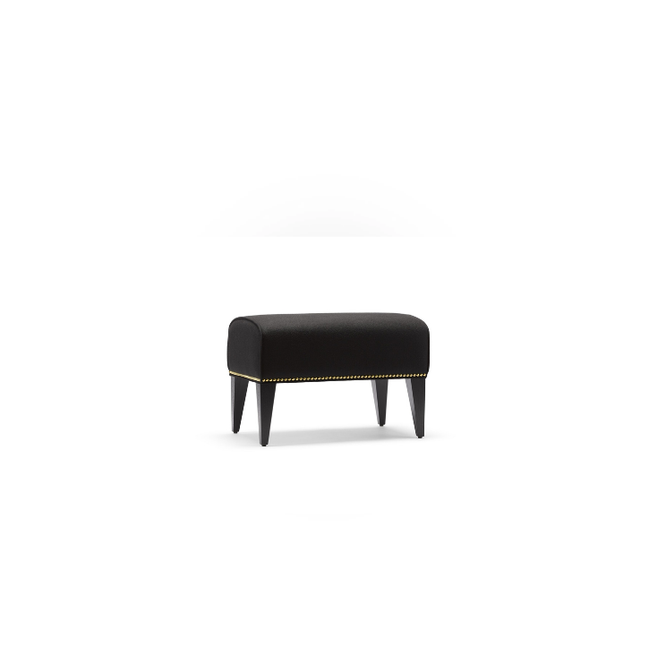 A black upholstered bench with four legs and gold nailhead trim on the bottom edge, placed against a plain white background.