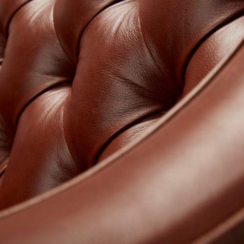 Close-up of a brown leather armchair with visible stitching and tufted design.
