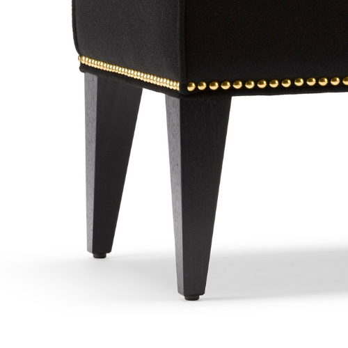 Close-up of a black upholstered chair with wooden legs and gold-colored nailhead trim.