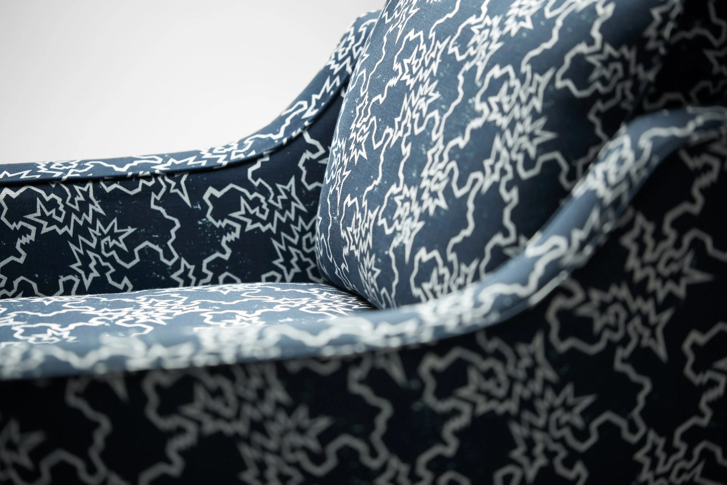 Close-up of a navy blue fabric with a white star and zigzag pattern, on the Reposer Chair.