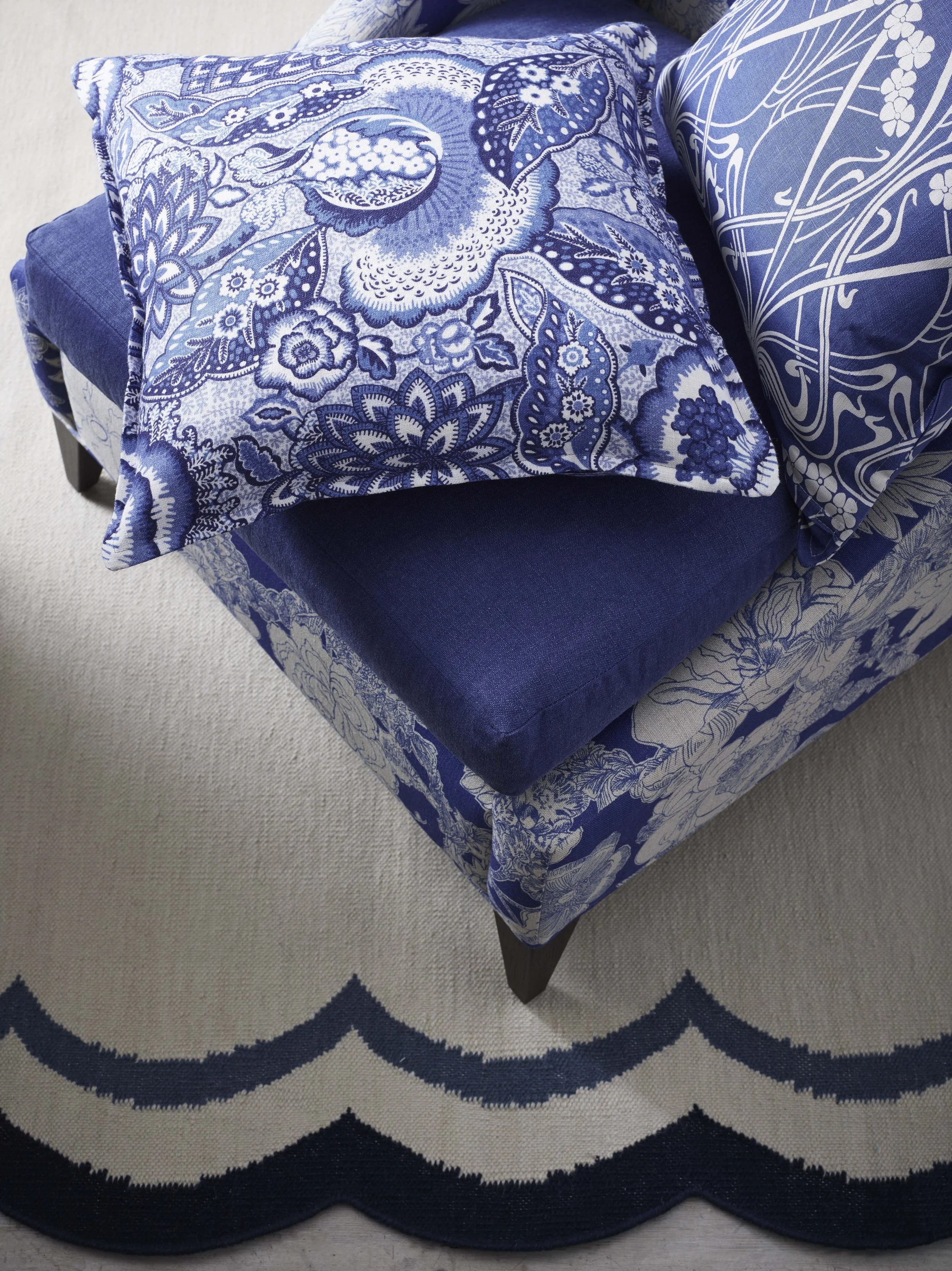 Close-up of a blue upholstered chair with two decorative pillows with blue and white floral patterns and a round blue and white rug underneath.