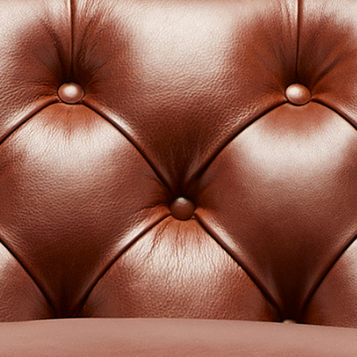 Close-up of a brown leather tufted chair with buttons.