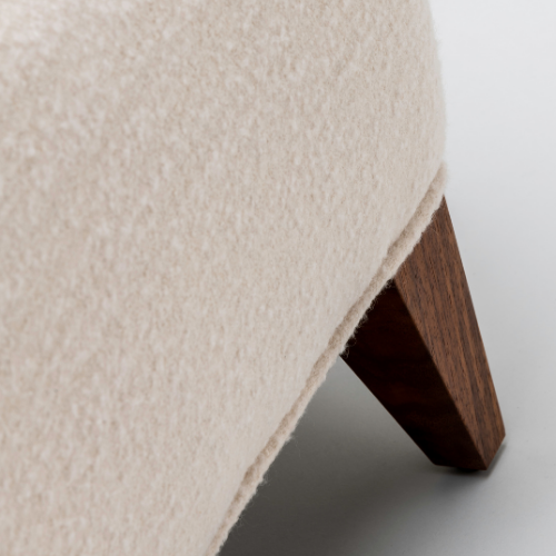 Close-up of the corner of a beige upholstered sofa showing a wooden leg.