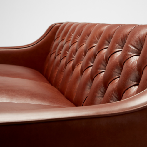 Close-up of a brown leather tufted sofa with a curved backrest.