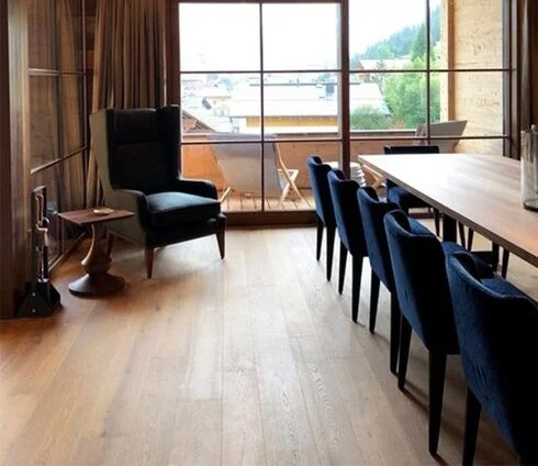 Spacious dining area with wooden flooring, a large window with a view, a dining table with six blue chairs, a high-back black armchair, and a small side table.