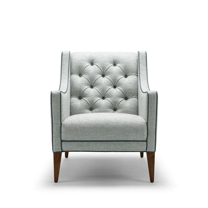 A light gray tufted armchair with wooden legs, set against a white background.