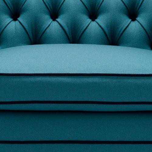 Close-up of a teal tufted sofa with button details and a cushioned seat.