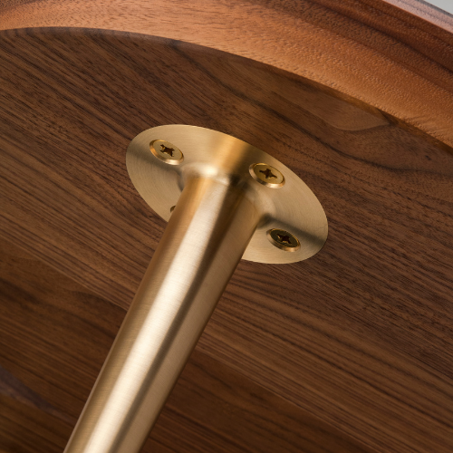 Close-up of a brass-colored metal leg attached to a wooden piece with screws.
