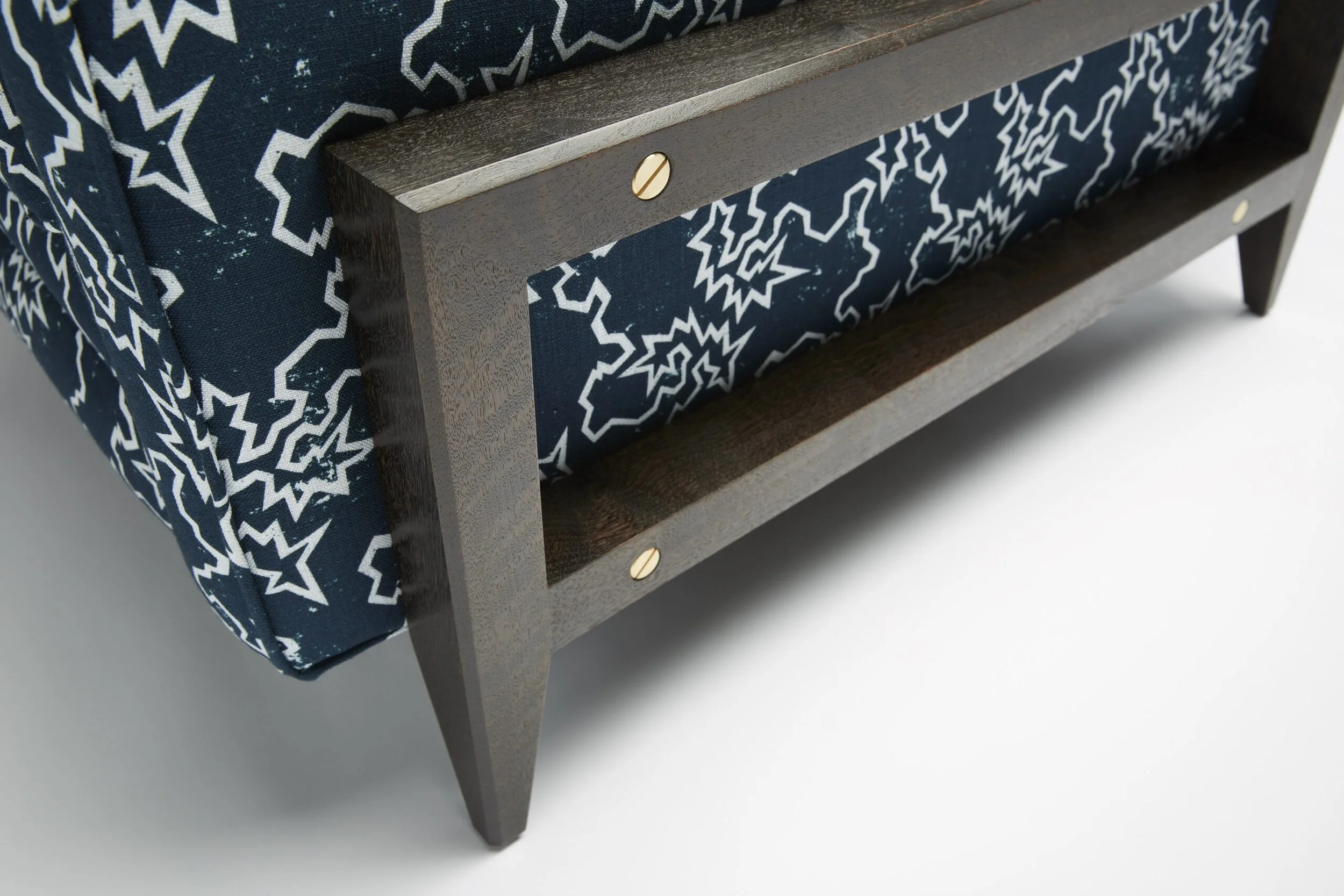 Close-up of a Reposer Chair with a dark wood frame, featuring a fabric cushion with a navy blue and white star pattern, and a section of the frame with a visible screw.