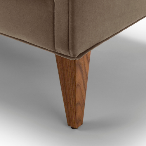 Close-up of a beige upholstered sofa with a wooden angled leg.