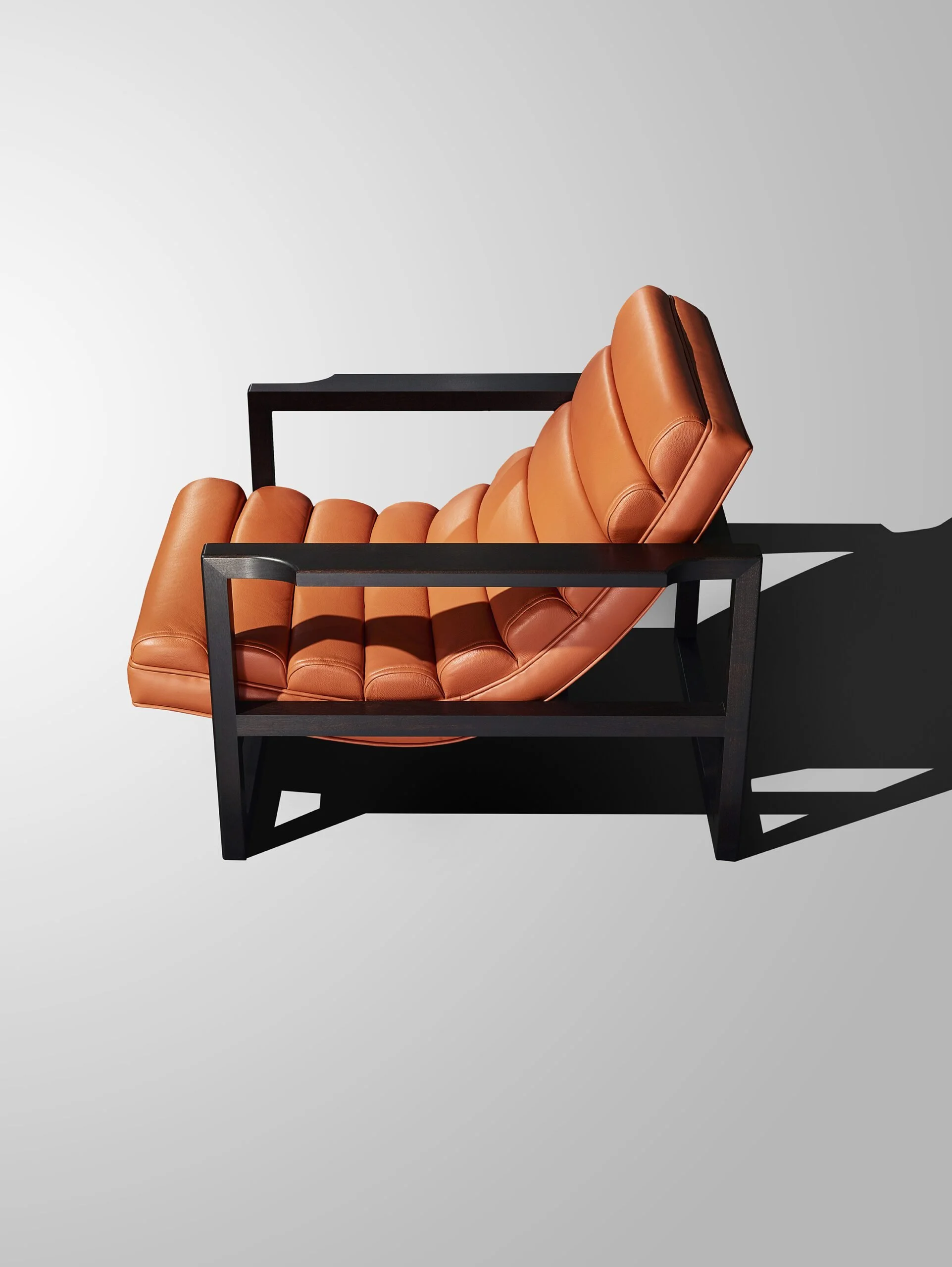A Florence Easy Chair  lounge chair with tan leather cushions and a black wooden frame against a light gray background.