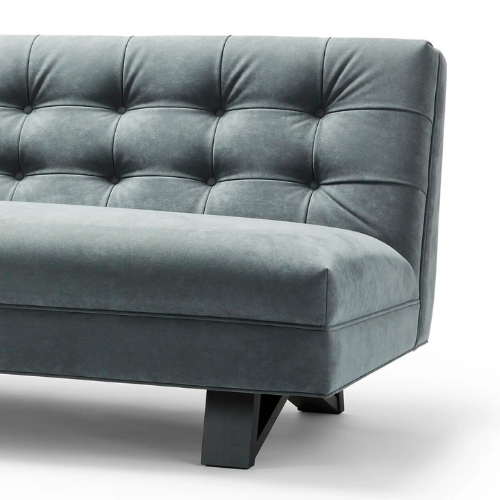 Partial view of a gray upholstered sofa with button-tufted backrest and wooden legs