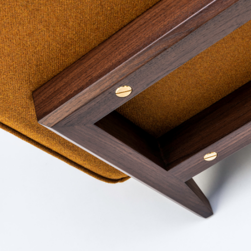 Close-up view of the corner of a modern wooden frame attached to a mustard-colored upholstered piece of furniture with gold screws.