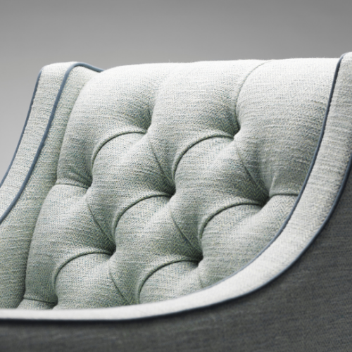 Close-up of a padded, tufted gray upholstered armchair with rounded edges.