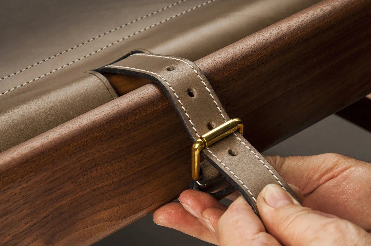 Close-up of a person adjusting a beige leather strap with white stitching around a wooden piece, secured with a brass buckle.