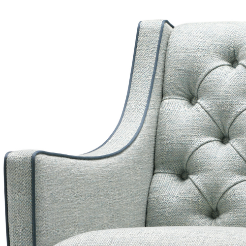 Close-up of a light gray upholstered armchair with button tufting and dark piping detail.