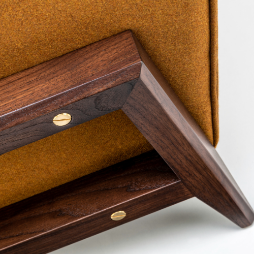 Close-up of a wooden piece of furniture with brass screws and orange fabric upholstery.