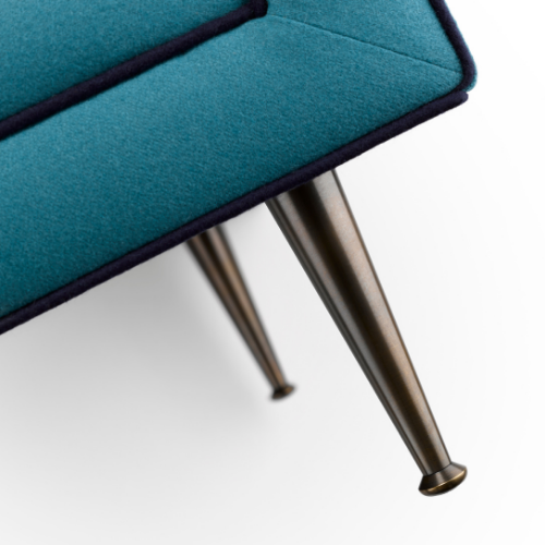 Close-up of a teal upholstered chair with black piping and metal tapered legs.