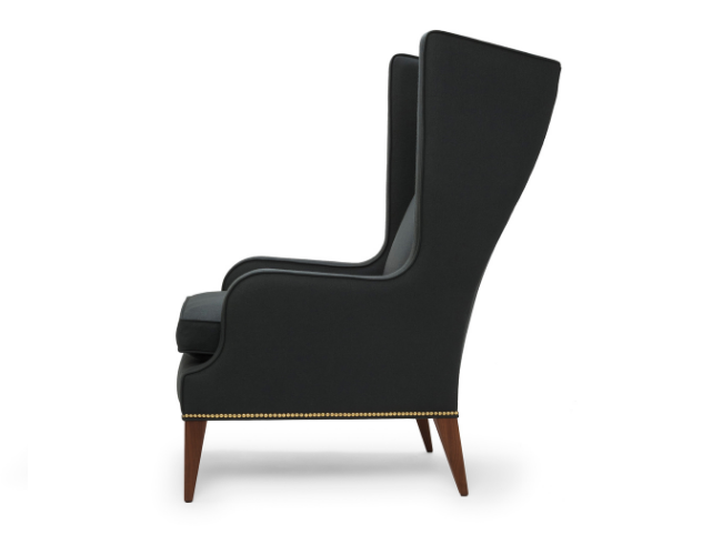 Black high-back armchair with wooden legs and nailhead trim, seen from the side.