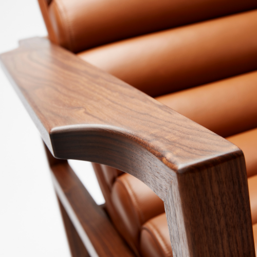 The Florence Easy Chair is a bare-wood constructed chair with a fluted leather seat in a light tan. The curved arm shown here.