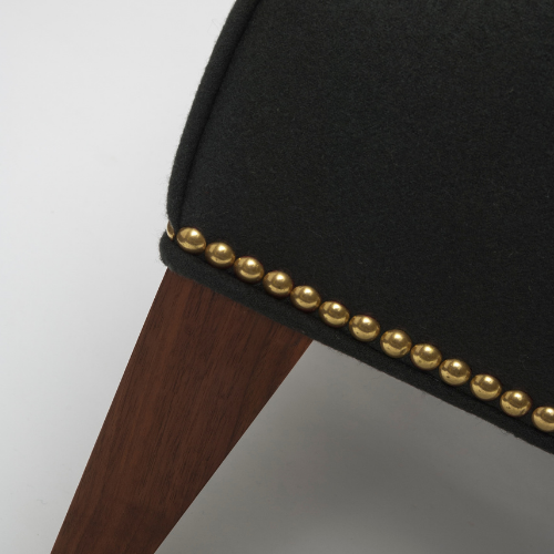 Close-up of a black upholstered chair with gold nailhead trim and a wooden leg.