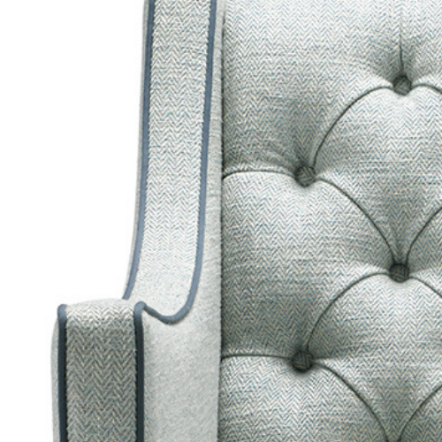 Close-up of a light blue upholstered armchair with tufted buttons and piping detail.