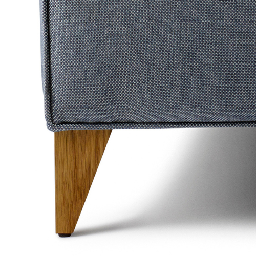 Close-up of a piece of furniture showing a gray fabric upholstered corner and a wooden leg.