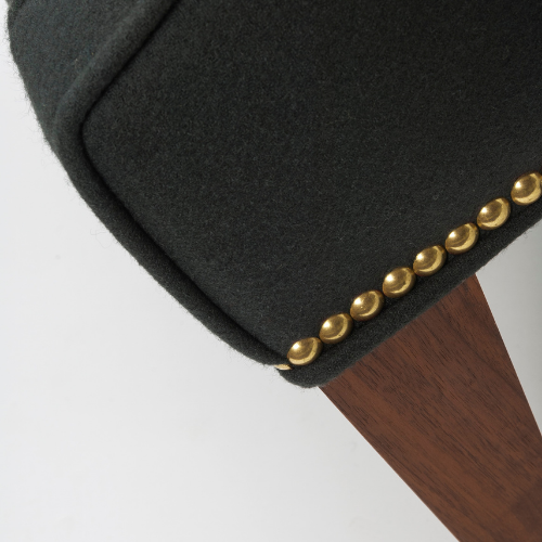 Close-up of a black upholstered chair with golden decorative studs on the edge, and a wooden leg.