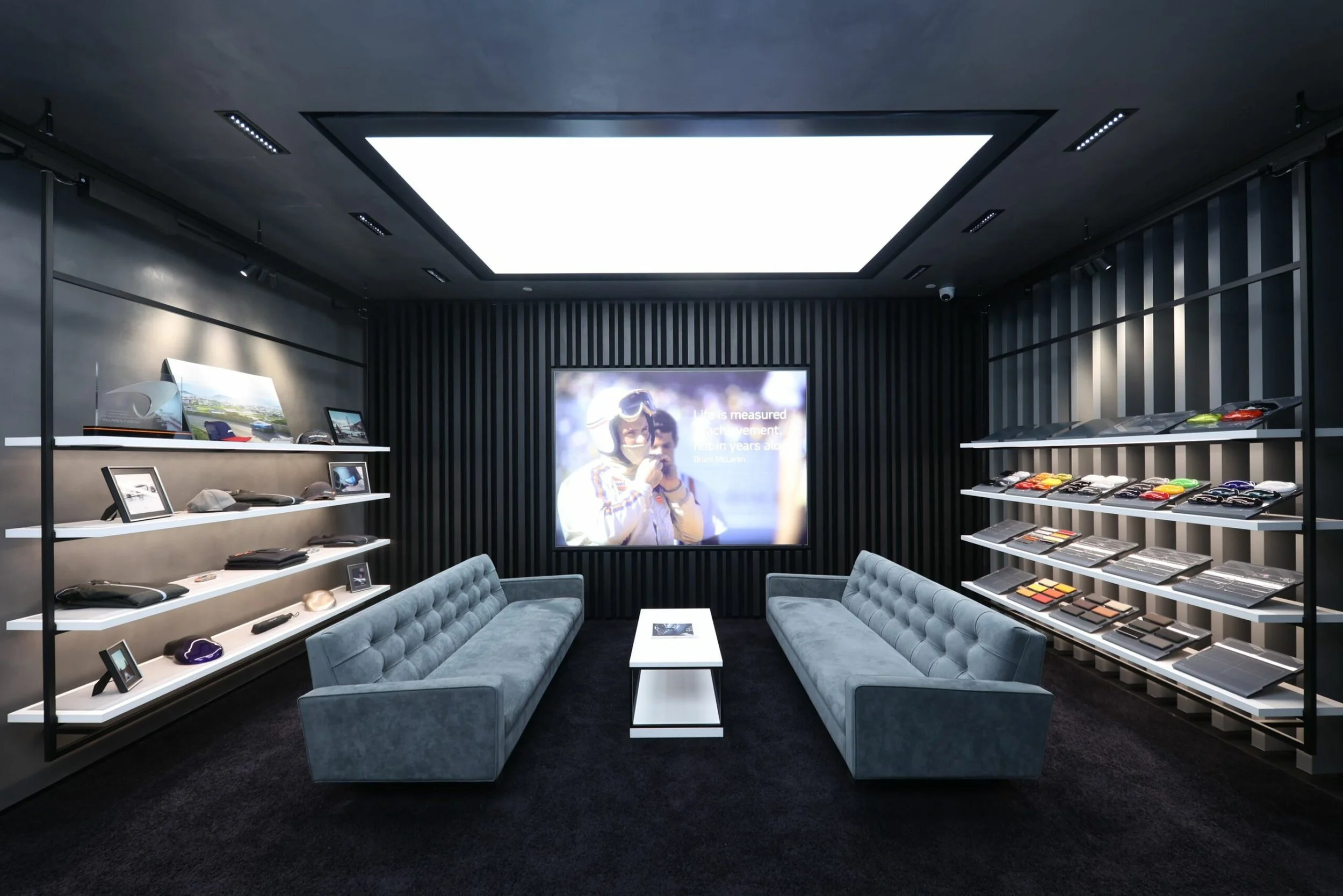 Modern retail store interior displaying sunglasses, hats, and makeup palettes with a seating area and a large screen.