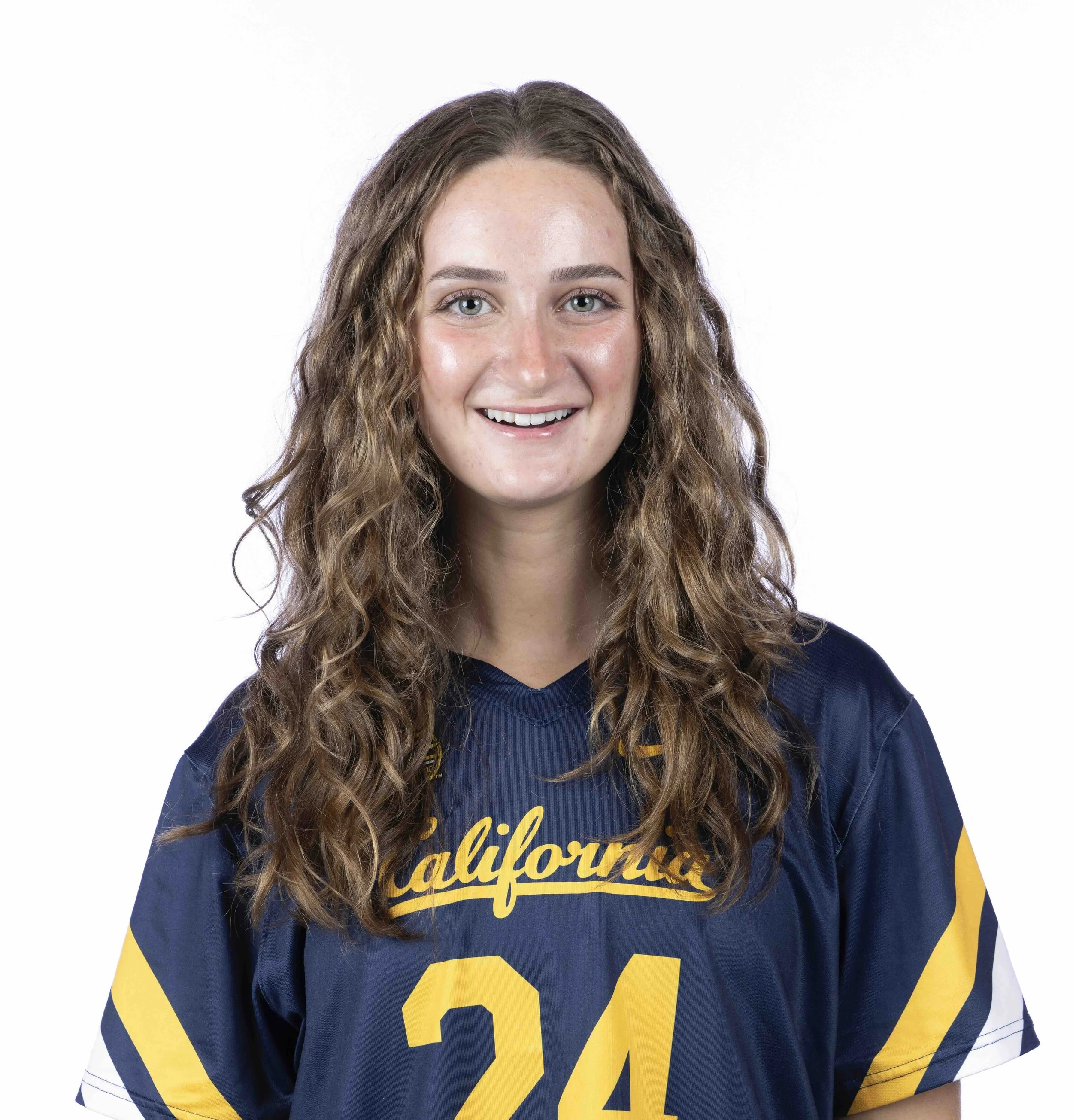 Close-up of a smiling young woman with curly brown hair, wearing a navy blue and yellow sports jersey with the text 'California' and the number 24 on it, against a plain white background.