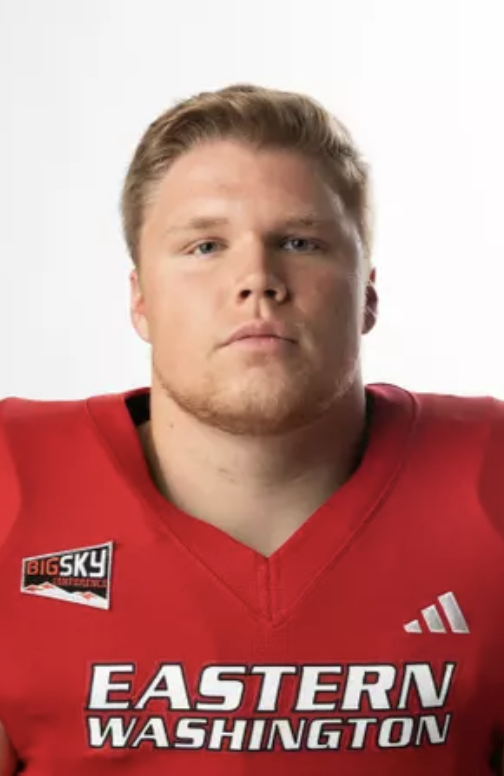 A young male football player wearing a red jersey with Eastern Washington and Big Sky Conference logos, looking serious.