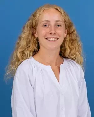 A young woman with curly blonde hair smiling against a blue background.