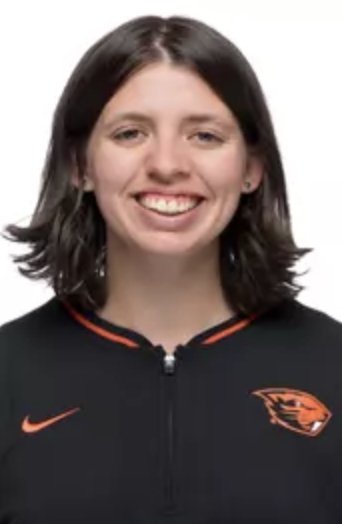 A young woman with shoulder-length dark hair smiling, wearing a black athletic jacket with orange accents, and a tiger logo on the chest.