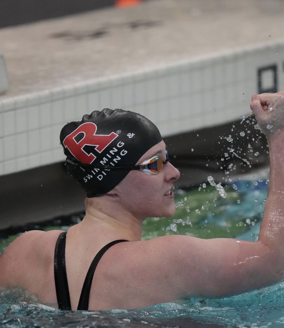 Swimmer wearing a black swim cap with a red 'A' and goggles, finishing a race in a swimming pool.