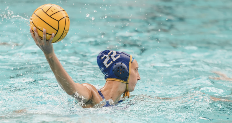 A water polo player wearing a blue cap with the number 22, holding a yellow water polo ball in the pool.