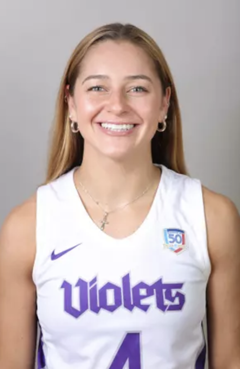 A young woman with long blonde hair, wearing a white basketball jersey with purple lettering, smiling at the camera.