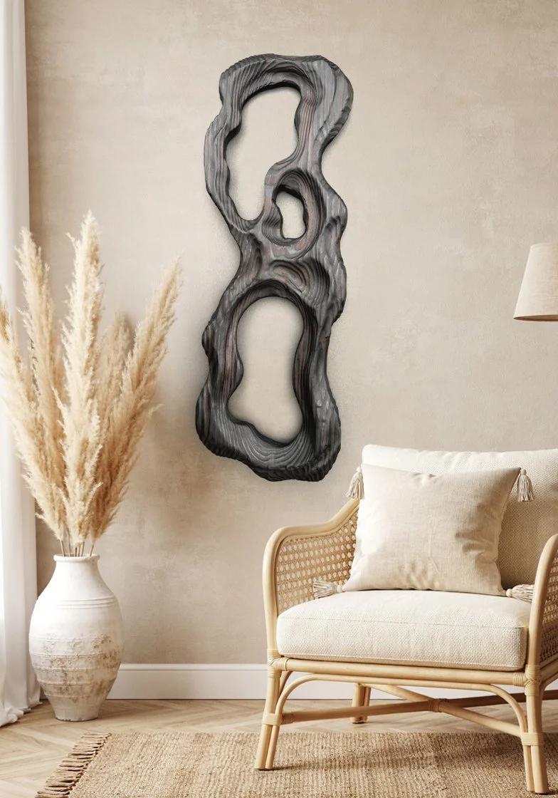 Modern living room with a beige armchair, throw pillow, tall vase with pampas grass, and an abstract wooden wall art piece.
