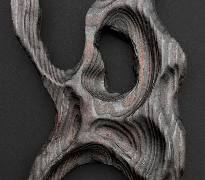Close-up of a layered, abstract wooden sculpture with irregular holes and a dark background.