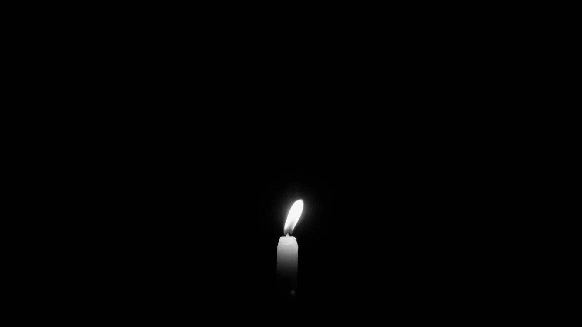 A single lit candle with a small flame against a dark background.