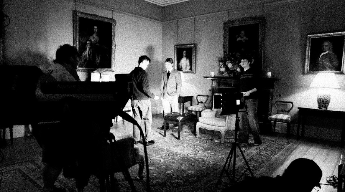 A black and white photo of a group of people in a room with paintings on the walls and various furniture.
