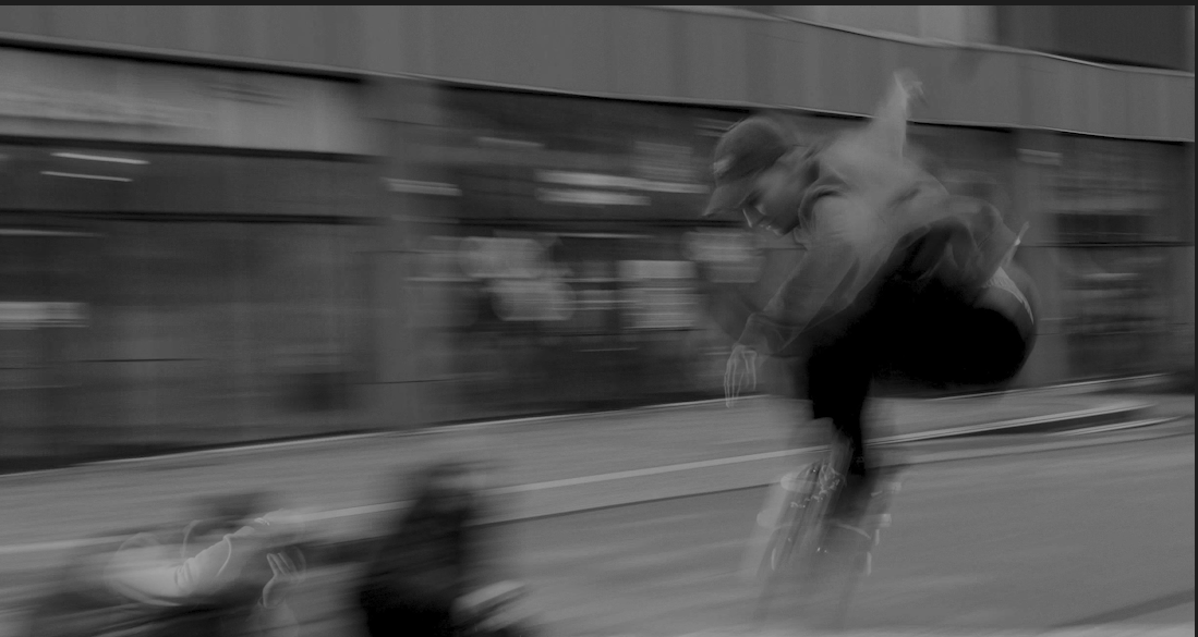 A person riding a bicycle quickly past a modern glass building on a city street, motion-blurred.