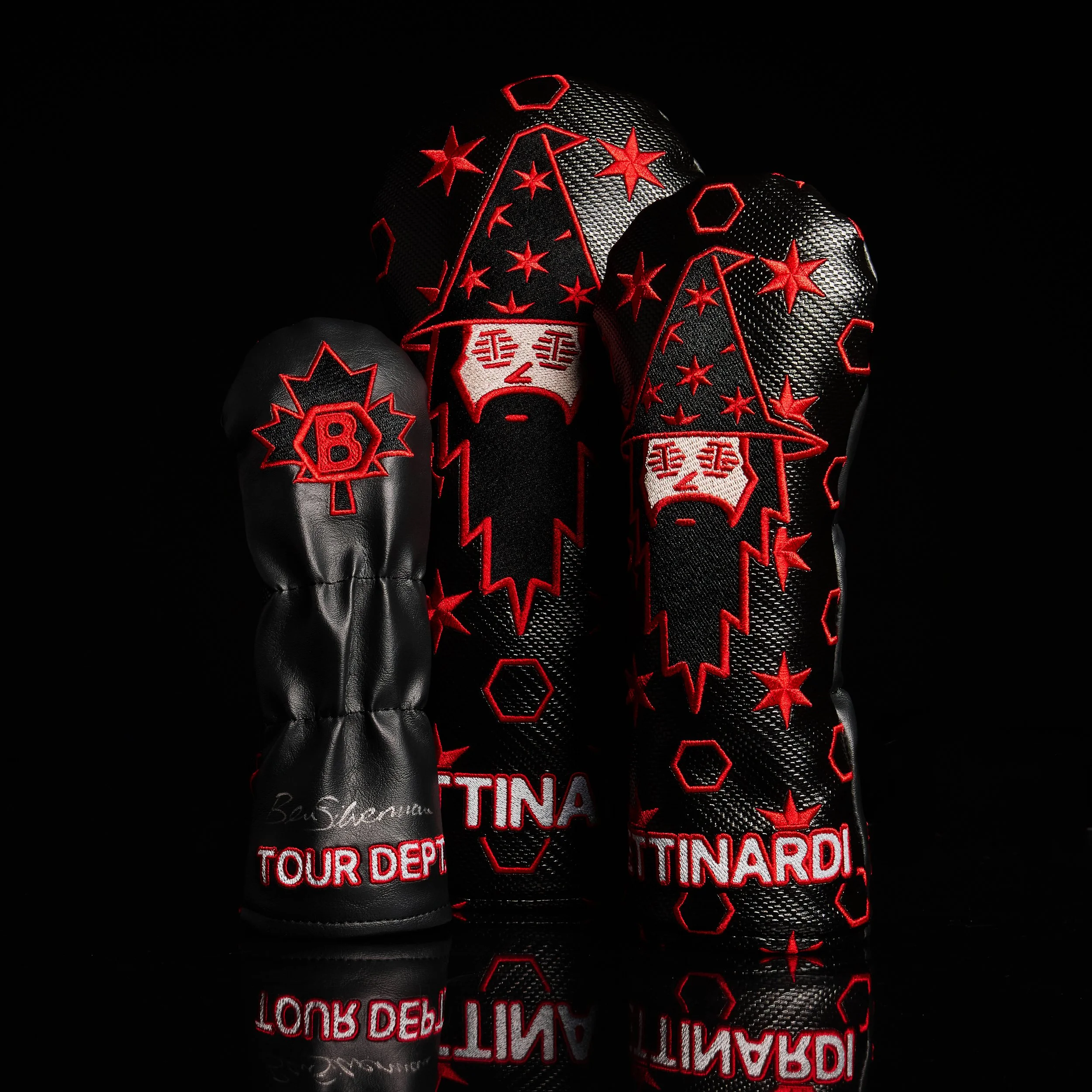 Set of black golf clubs with red and white embroidered logos and text, arranged on a reflective black surface.