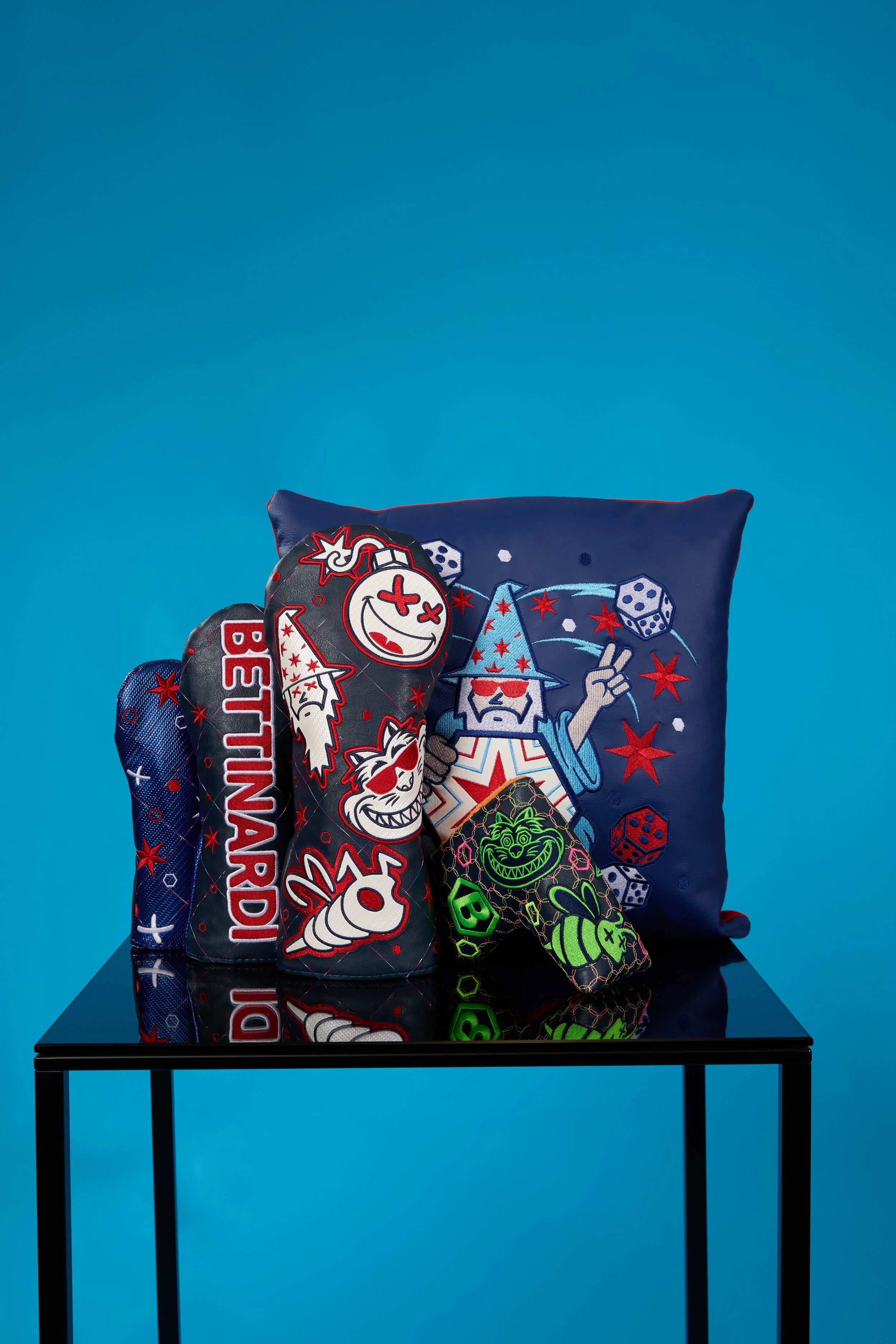 A blue pillow with embroidered cartoon characters, stars, and dice sitting on a black table against a blue background.