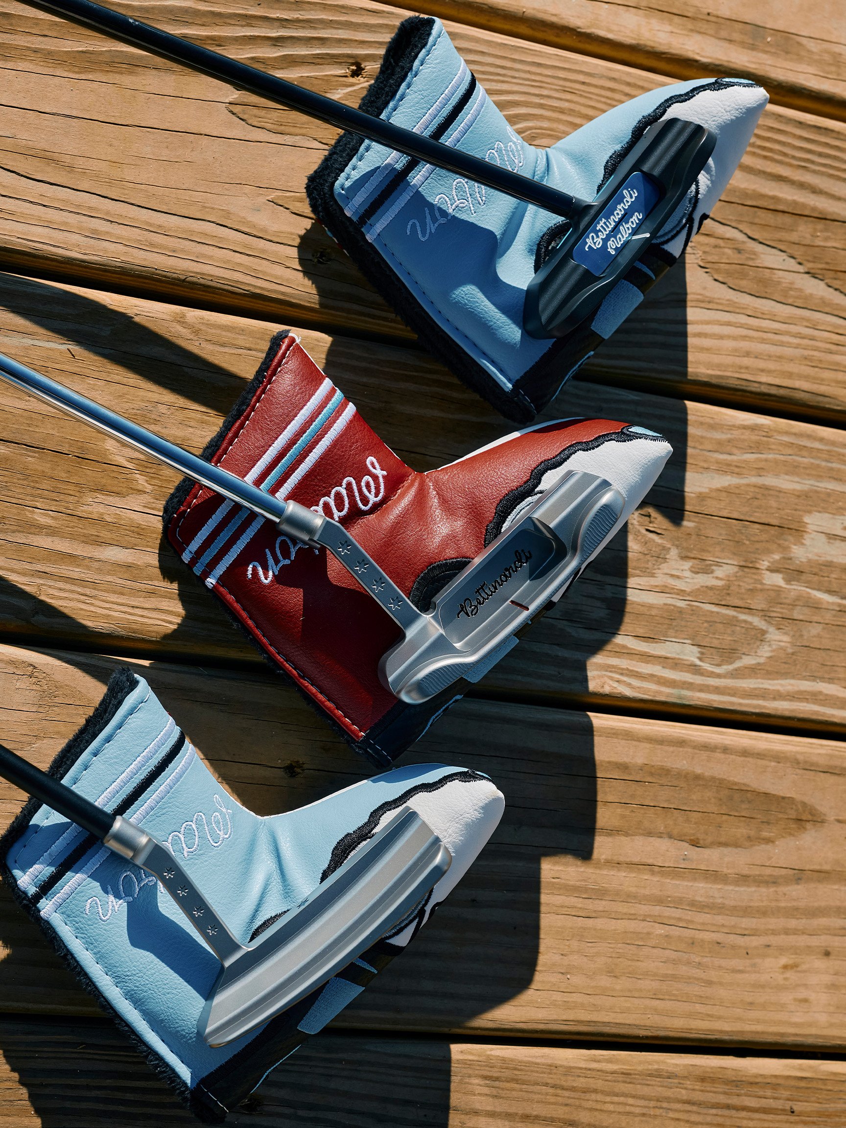 Two golf putters with headcovers, one red and one blue, resting on a wooden surface outdoors.