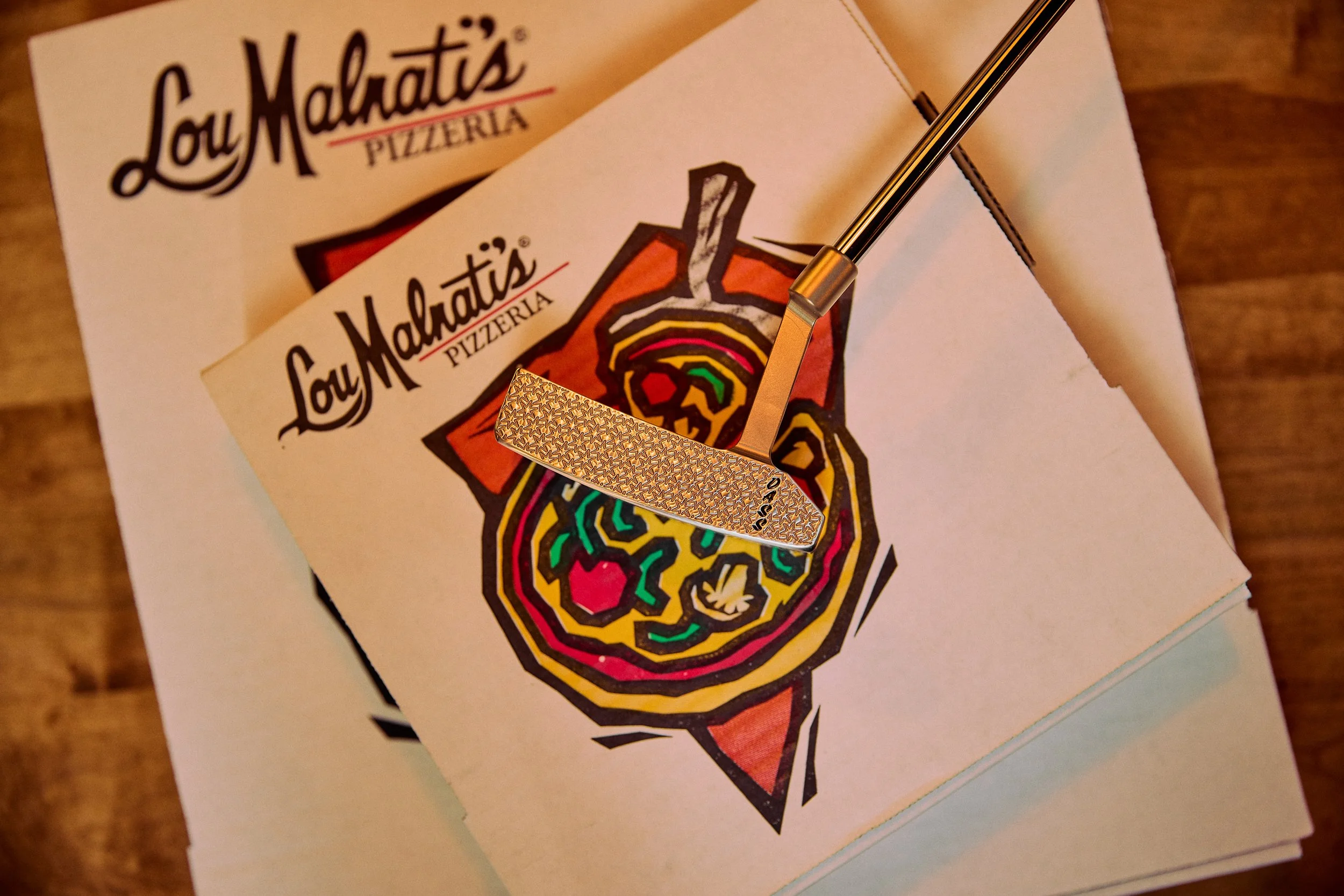 A colorful, stylized drawing of a roasted chicken on a plate, with a rainbow-colored outline, is placed on top of a napkin. The napkin features a logo with the text 'Lou Malnati's Pizzería' and an illustration of a tornado with a rainbow outline.