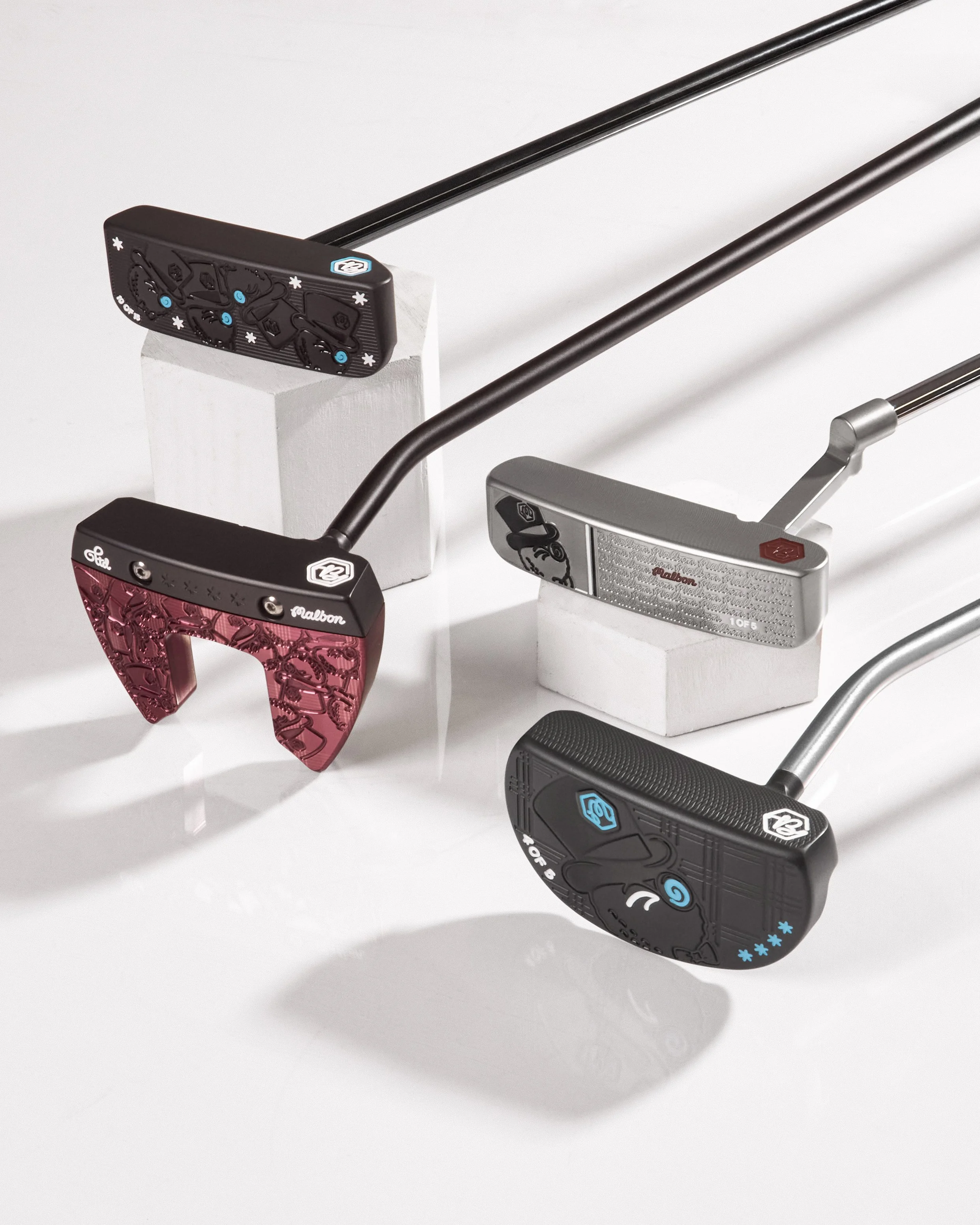 Multiple golf putters with decorative, jeweled handles displayed on white blocks against a white background.