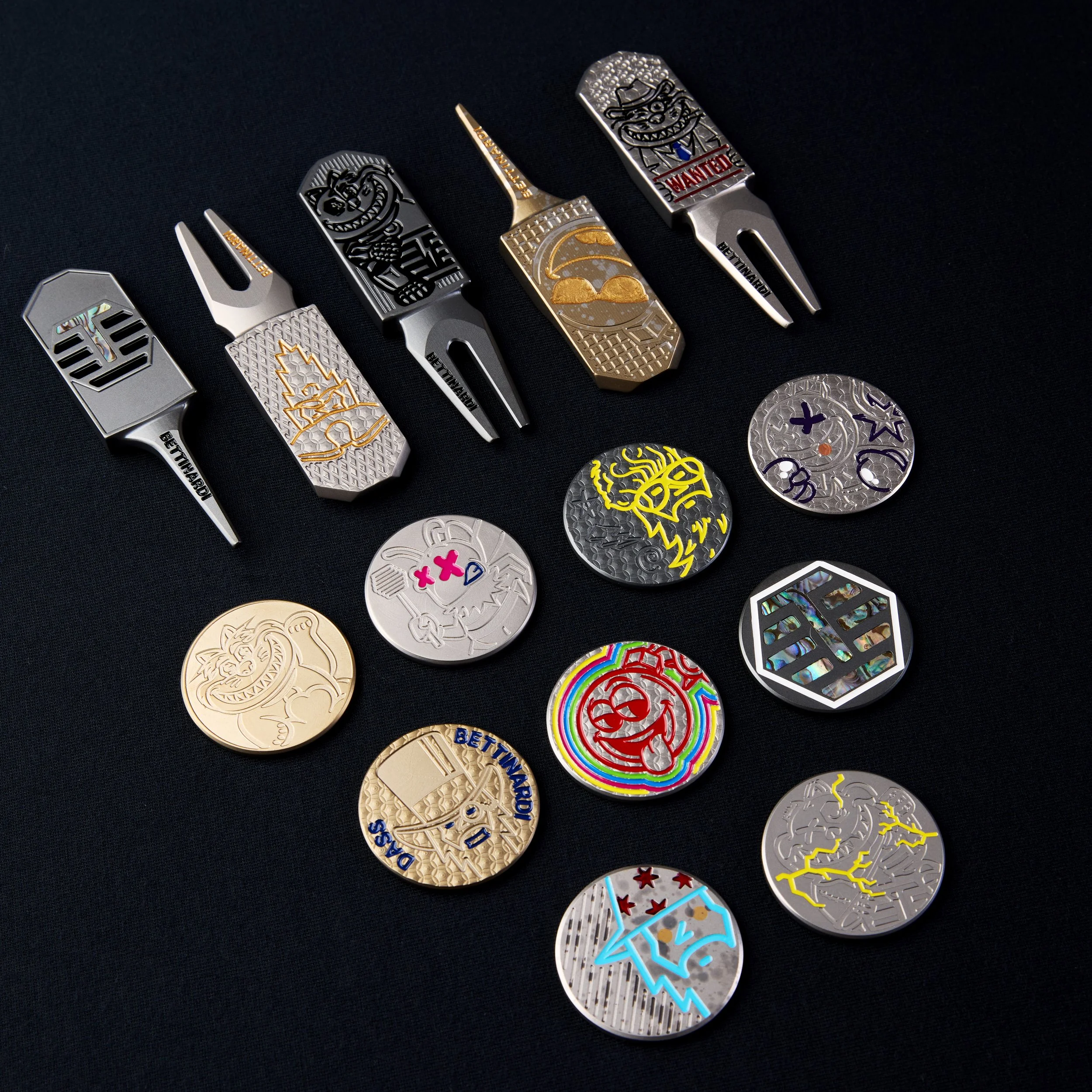 Collection of colorful, decorative metal golf divot tools with various engraved designs and logos, placed on a black background.