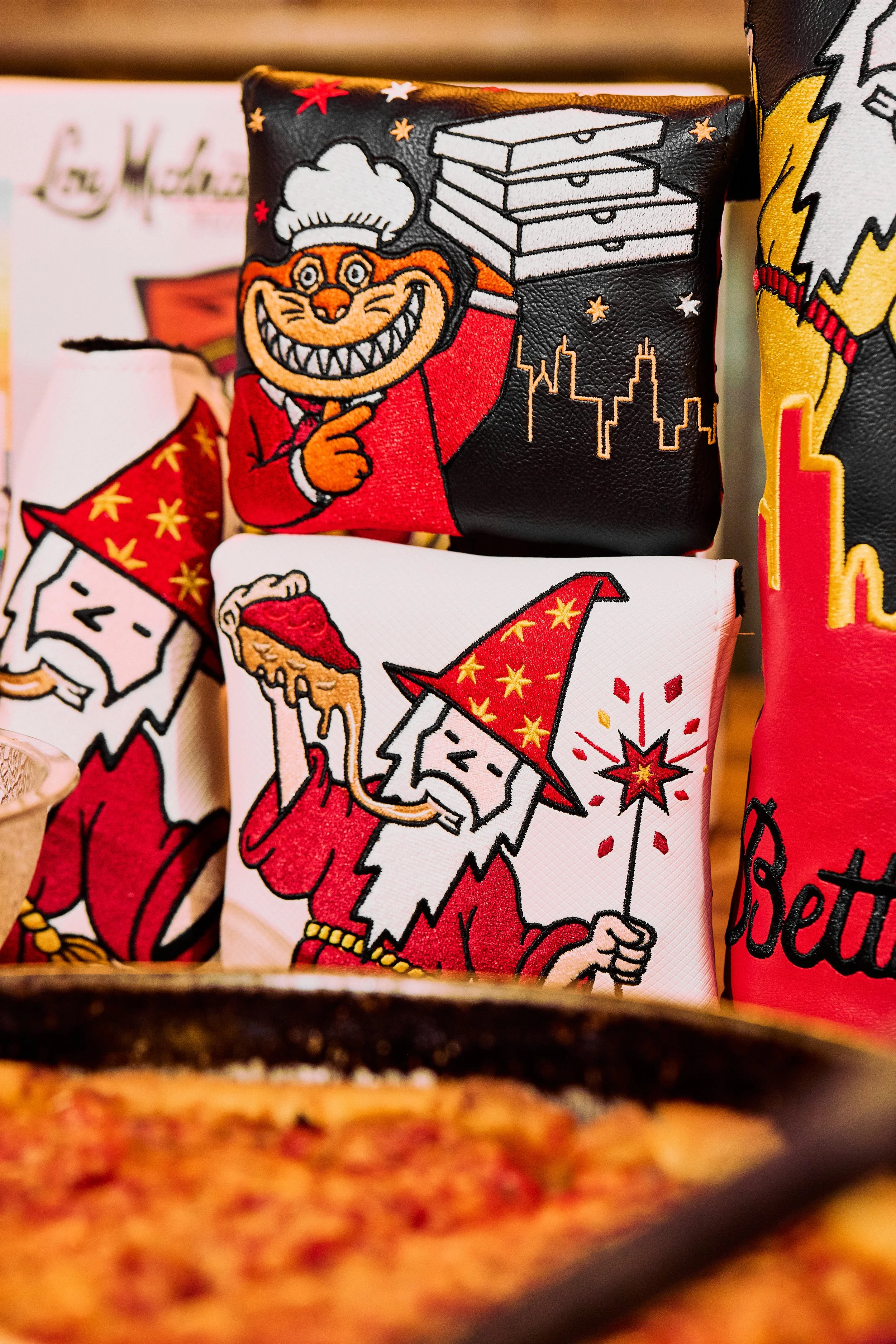 Close-up of embroidered patches featuring festive designs, including a grinning cat chef holding a tray, a snowman, and other holiday-themed images, with a blurred background.